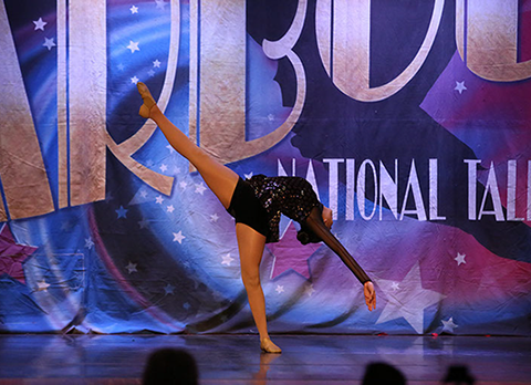 A girl onstage at Starbound National Talent Competition doing a layout. She is wearing a dark glittery costume. This is a jazz dance.
