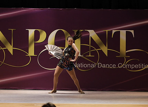 A girl on stage at Starbound National Dance Competition with a dark glittery costume and a fan. This picture is from a jazz dance.