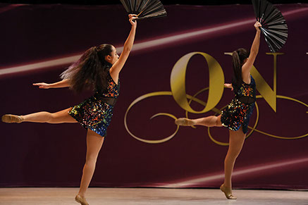 Two girls on stage at On Point Dance Competition in "oilslick" costumes, holding fans and doing an attitude. This picture is from a jazz dance.