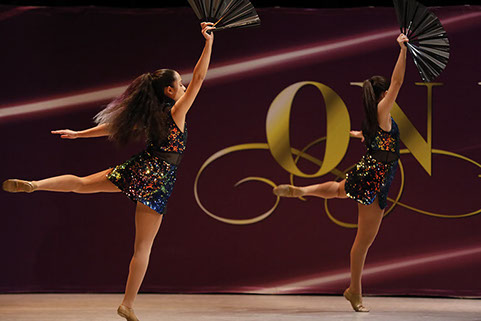 Two girls on stage at On Point Dance Competition in "oilslick" costumes, holding fans and doing an attitude. This picture is from a jazz dance.