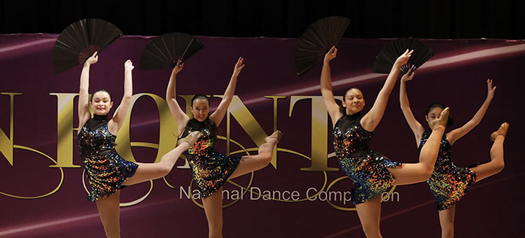 Four girls on stage at OnPoint Dance Competition in "oilslick" costumes and holding fans, doing an attitude. This picture is from a jazz dance.