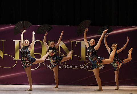 Four girls on stage at OnPoint Dance Competition in "oilslick" costumes and holding fans, doing an attitude. This picture is from a jazz dance.