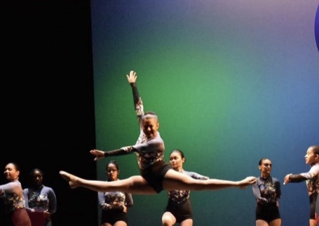 Various girls on stage at Kean University in purple and black costume. One girl is midair doing a perfect leap.